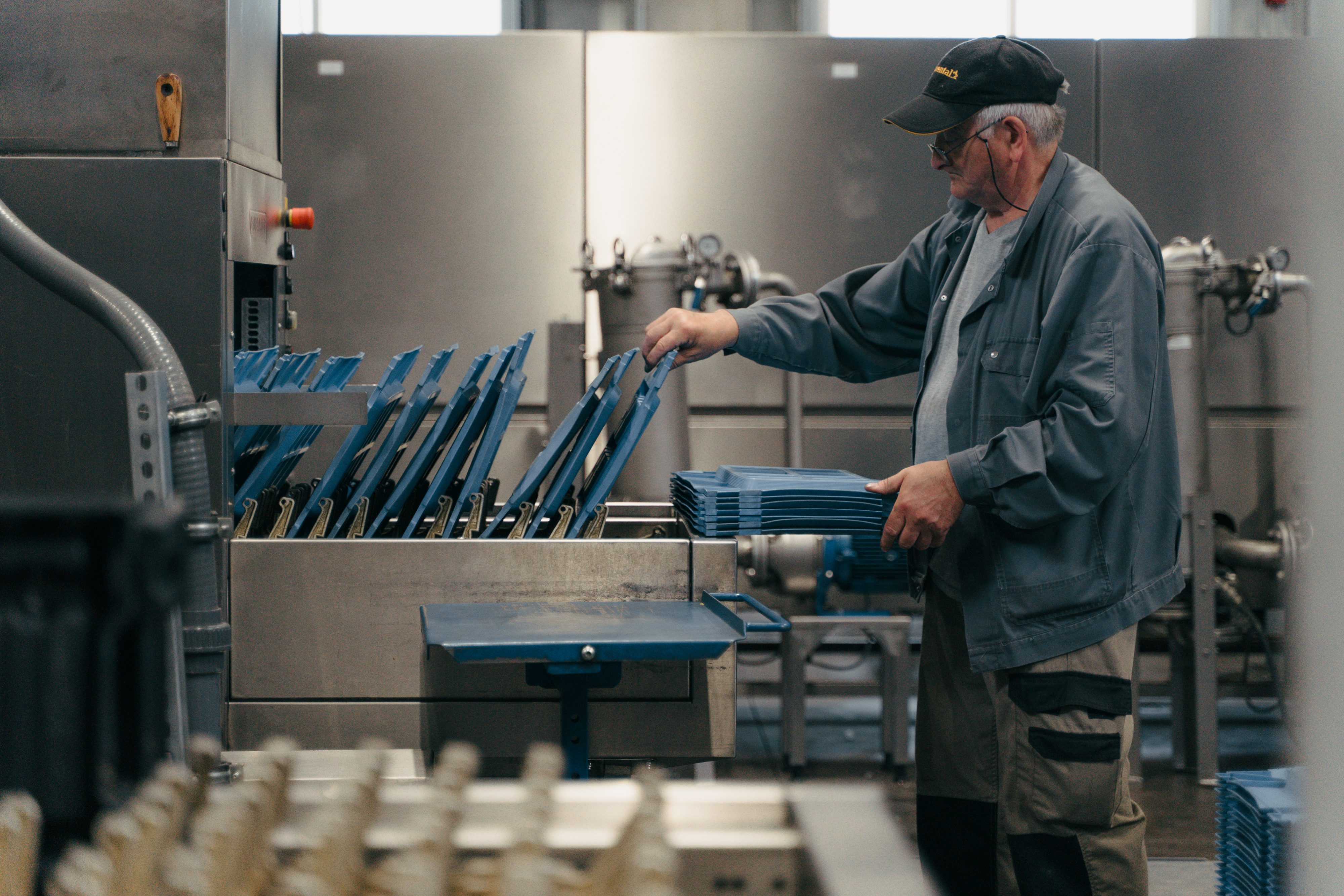 Mitarbeiter legt blaue Kunststoffteile in eine industrielle Reinigungsmaschine.
