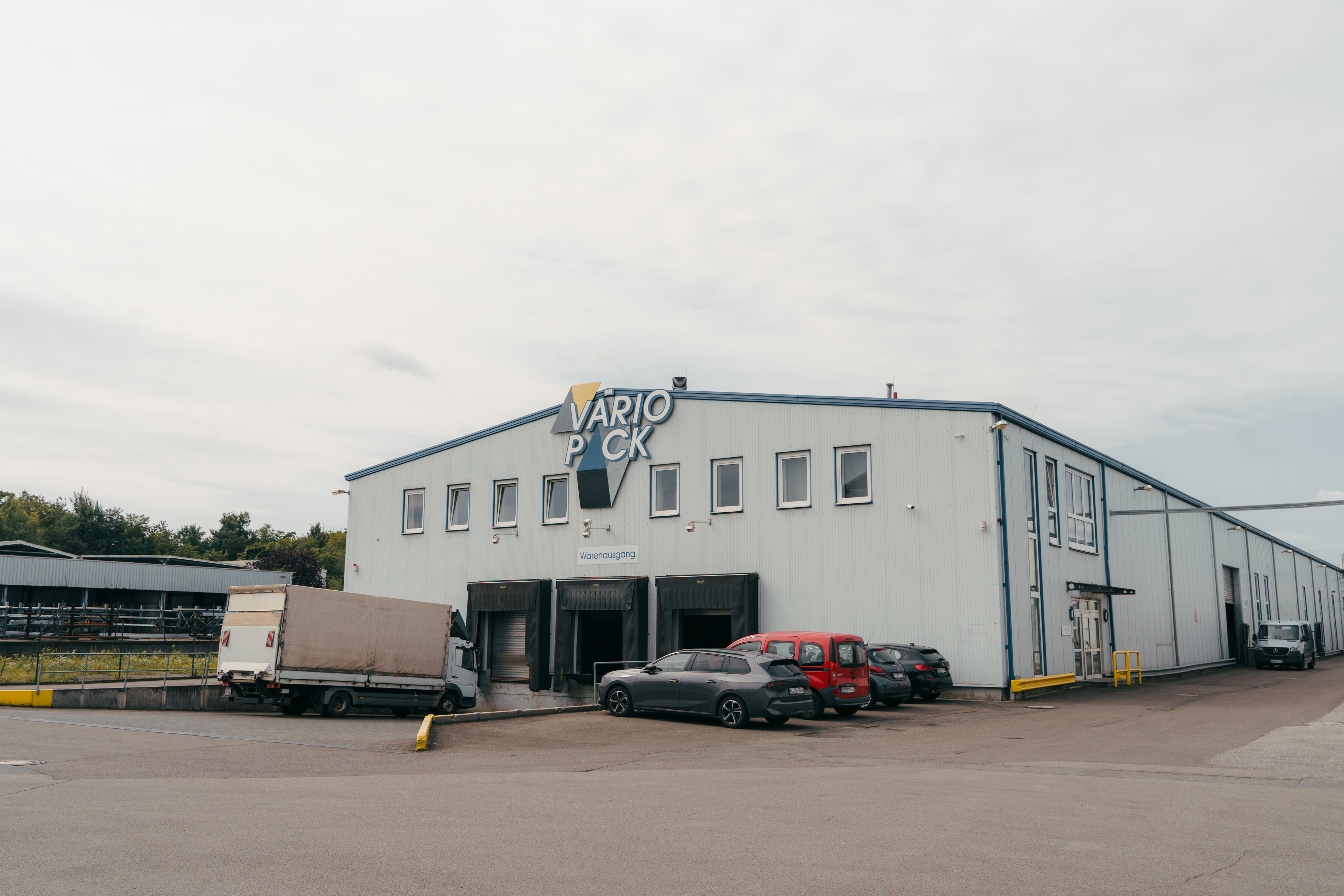 Eingangsbereich des Variopack-Gebäudes mit Firmenlogo und geparkten Fahrzeugen.
