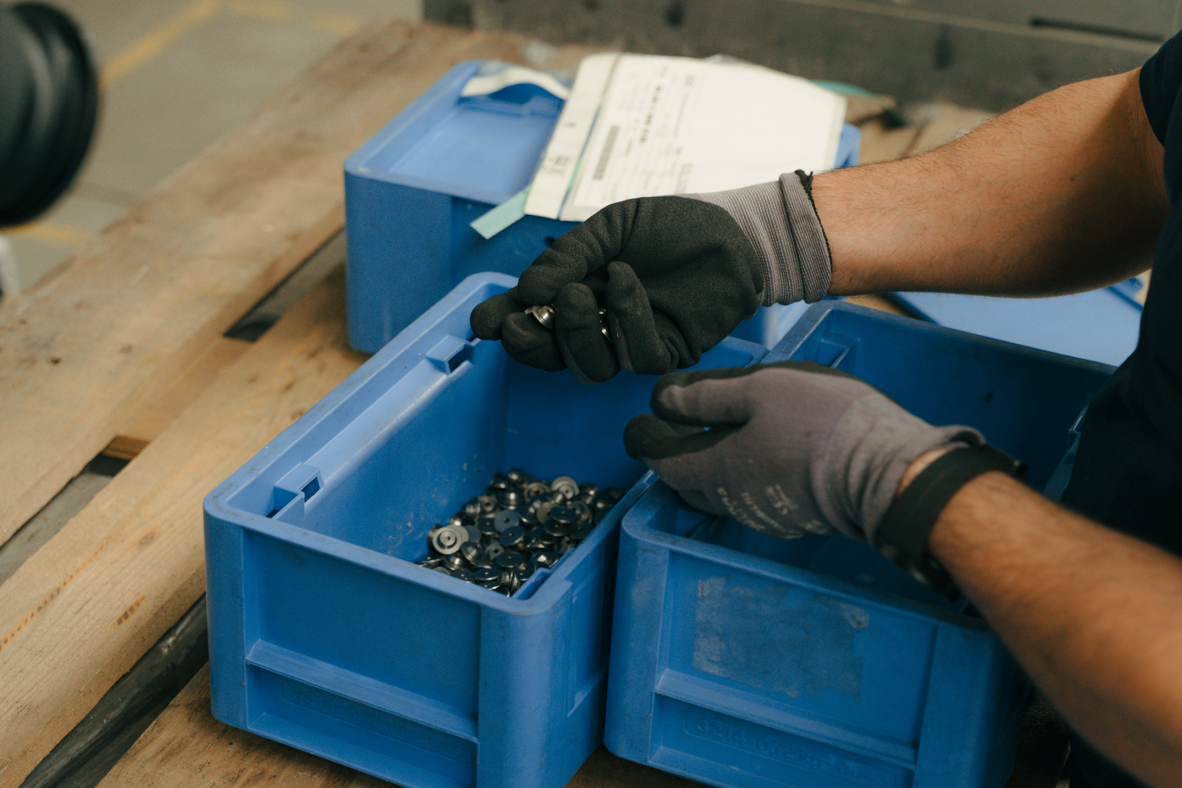 Mitarbeiter sortiert Kleinteile in blauen Boxen auf einer Werkbank.